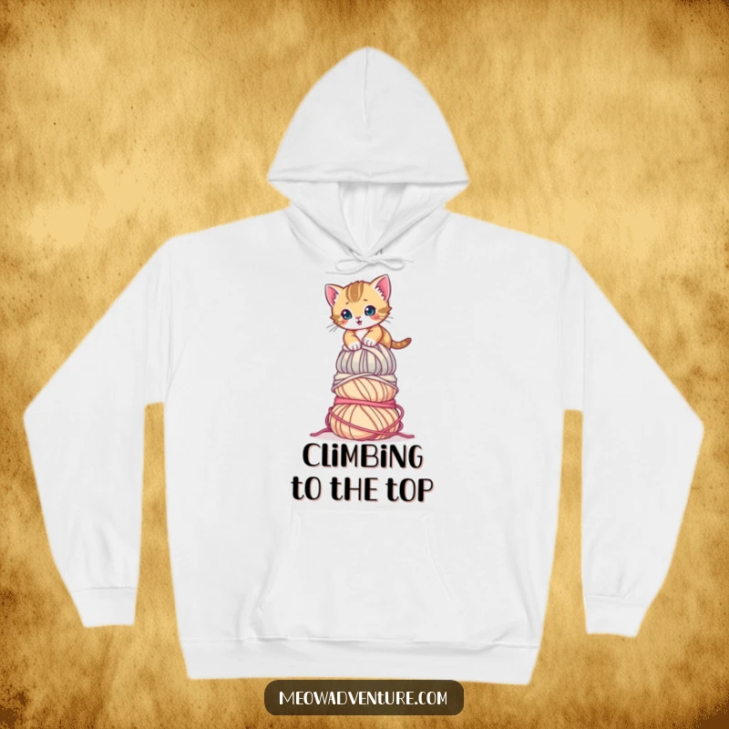 Funny Determined Kitten Hoodie showing a focused kitten ascending a massive mountain of yarn. A warm, humorous, and inspiring top.